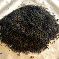 Close-up of loose Assam black tea leaves piled on parchment showing fine dark twisted leaves ready for brewing