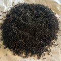 Close-up of loose Lapsang Souchong black tea leaves from Fujian province, dark and finely twisted on parchment paper.
