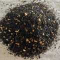 Close-up of The Grey Lady loose black tea blend with dark leaves, bergamot, and bright orange peel pieces on parchment paper