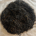 Close-up of loose Scottish Breakfast black tea leaves showing dark, twisted leaves with golden tips on a light background