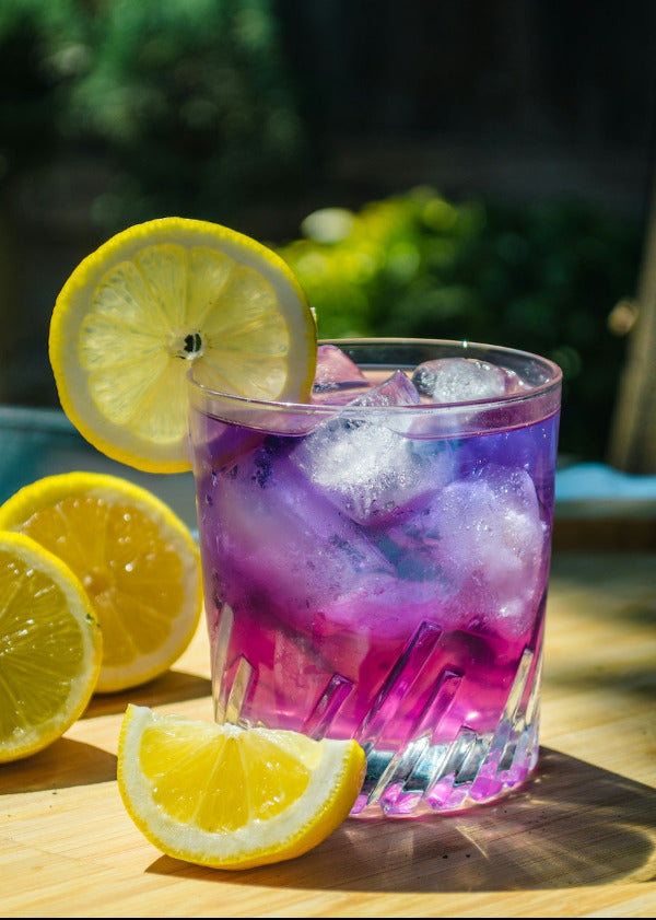 Glass of purple lemonade with ice and lemon slices on a wooden surface.